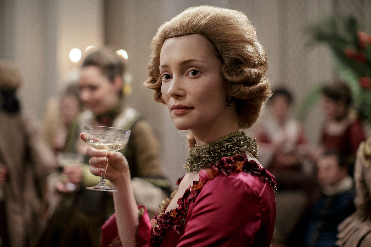 Lotte Verbeek as Geillis Duncan in 'Outlander' Season 3. She wears a magenta gown with a strawberry blonde, women's style colonial wig and holds a glass of champagne in her hand. Geillis Duncan was in 'Outlander' Season 1, 2, and 3, and given her time traveling abilities, she could be part of 'Outlander' Season 6.