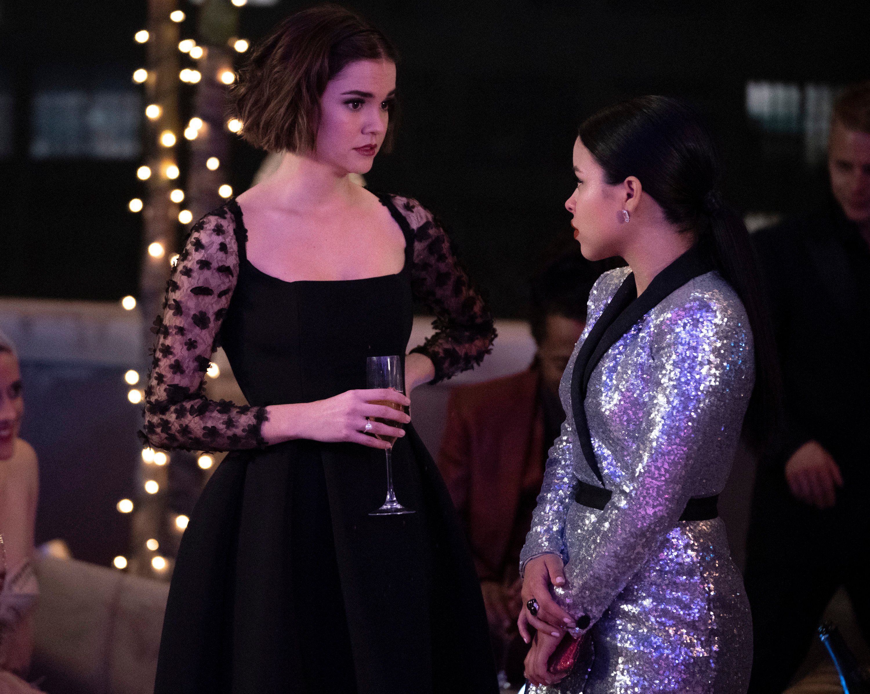 Callie holds a glass of wine and talks to Mariana at a holiday party