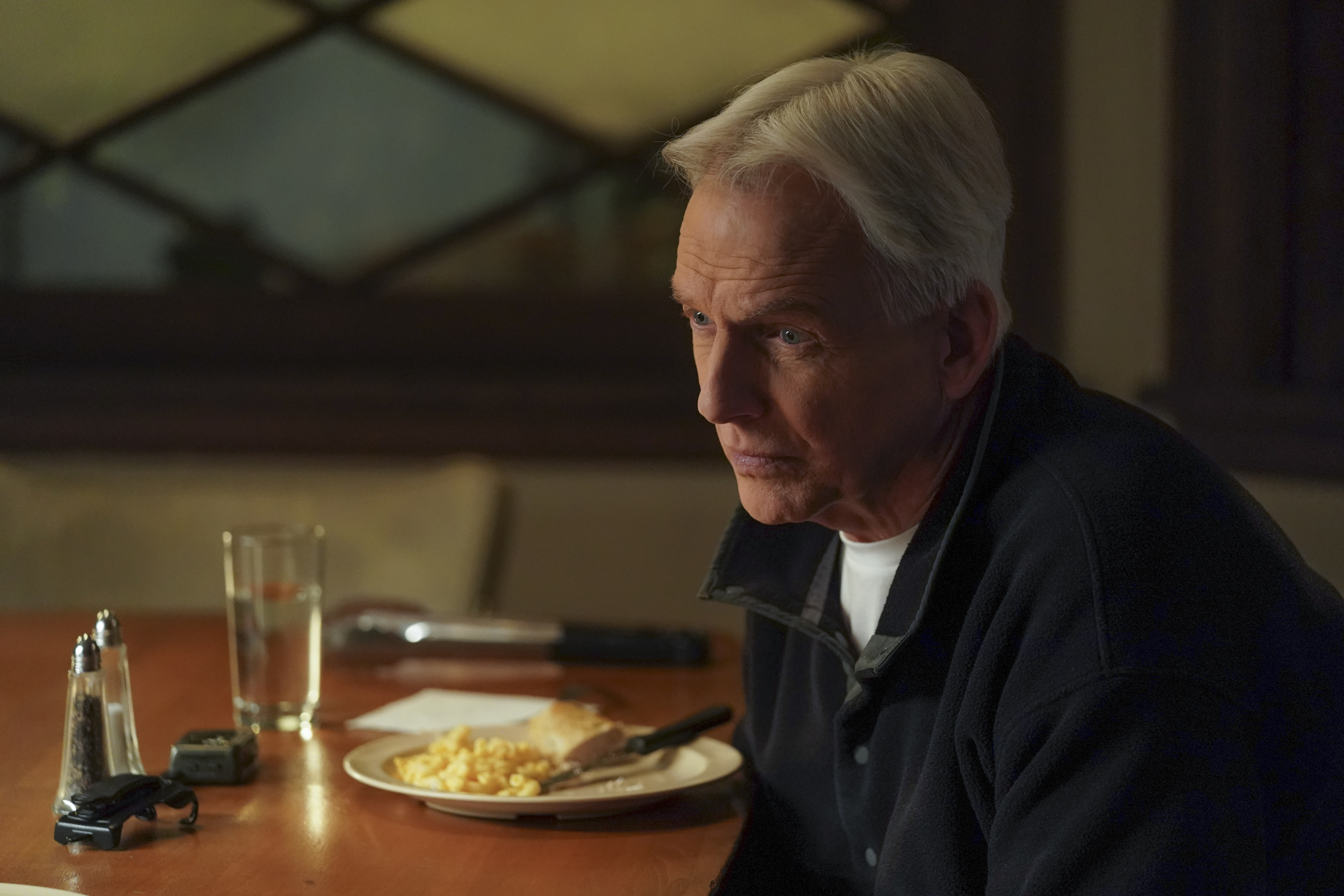 Mark Harmon sitting in front of a plate of food on 'NCIS.'