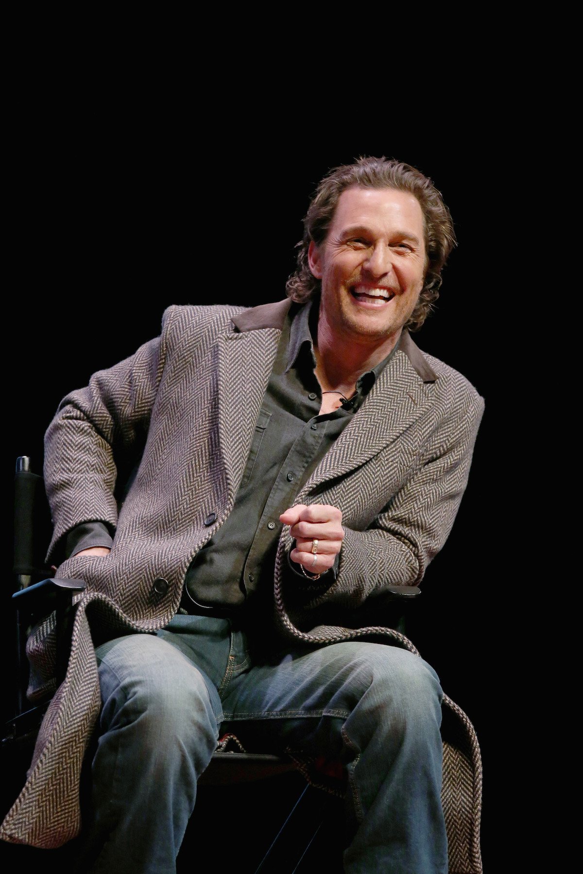 Matthew McConaughey sits on stage in a brown patterned coat , as he smiles to an audience on stage