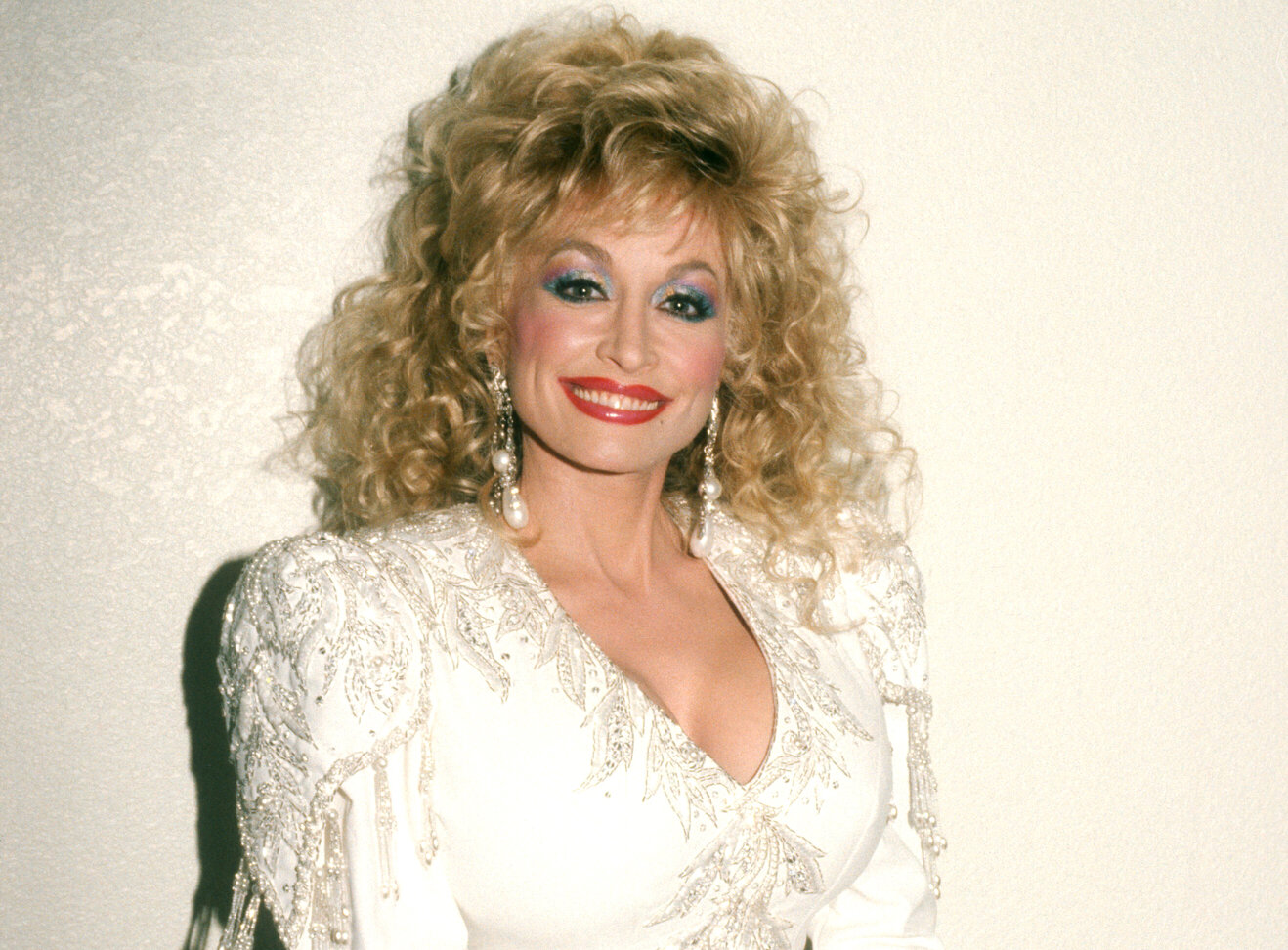 Dolly Parton poses for a portrait in a white dress in 1988.