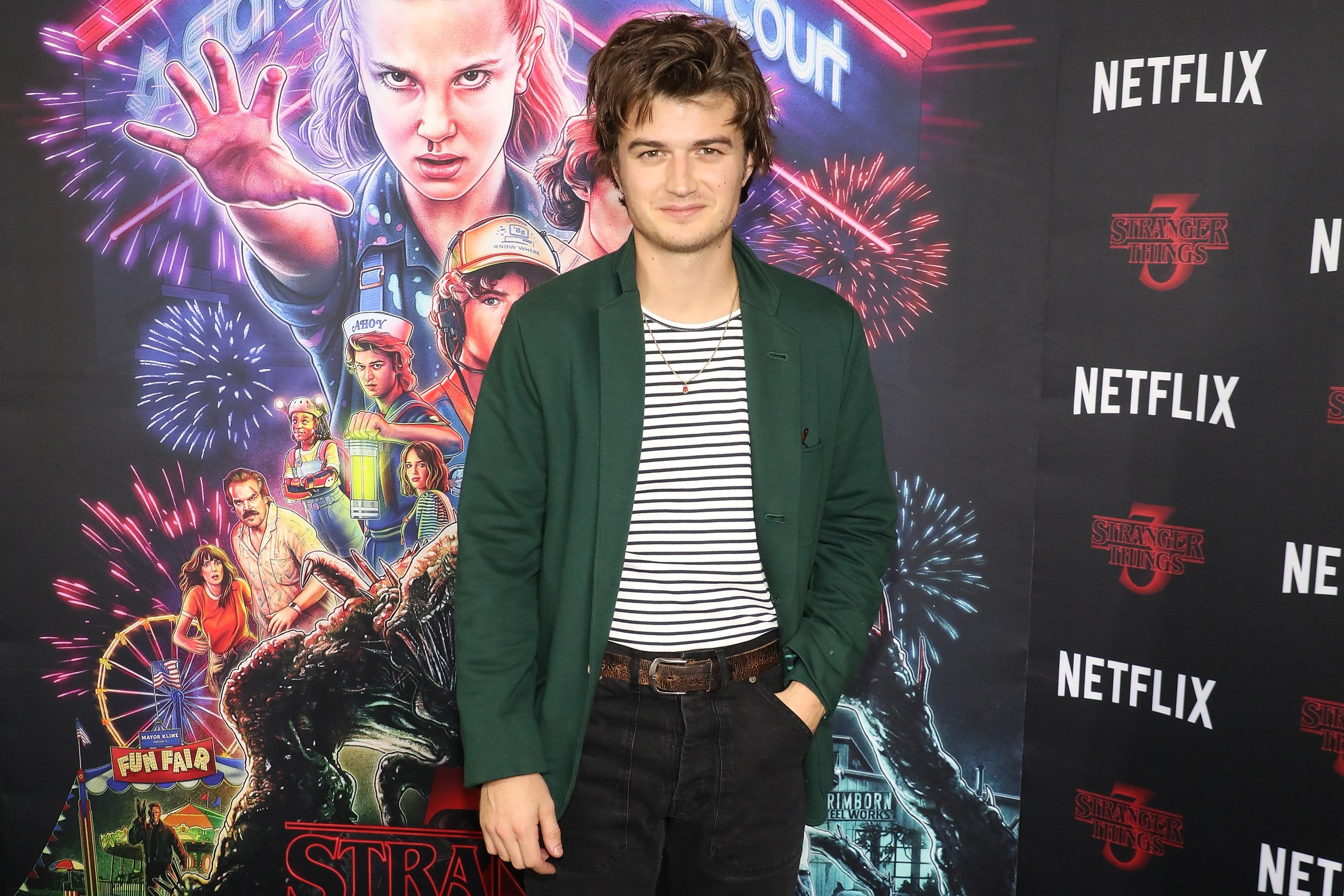 'Stranger Things' starJoe Keery wearing a green jacket, a black and white striped shirt, and black jeans at a screening of Season 3.