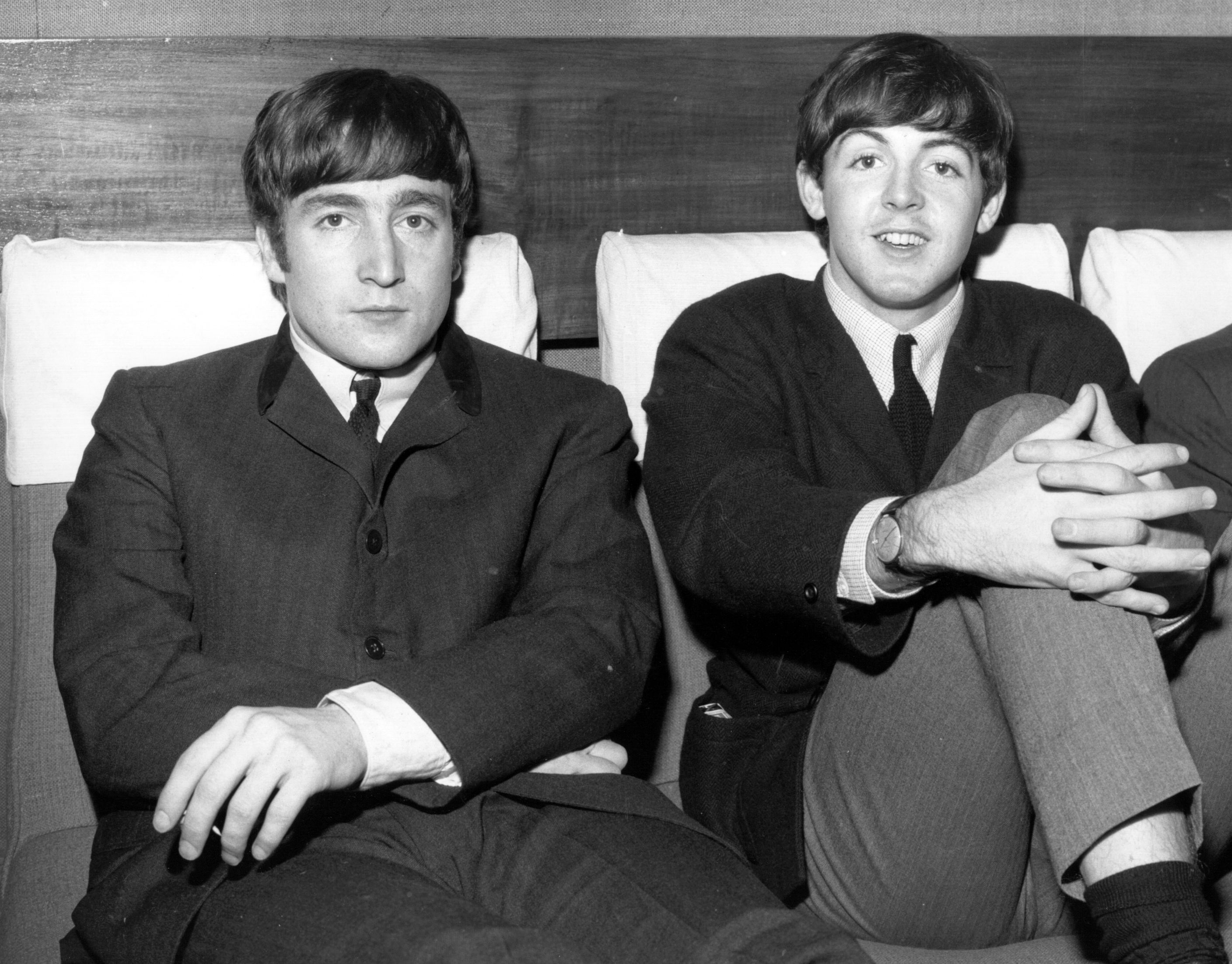 John Lennon and Paul McCartney of The Beatles sitting next to each other and wearing suits