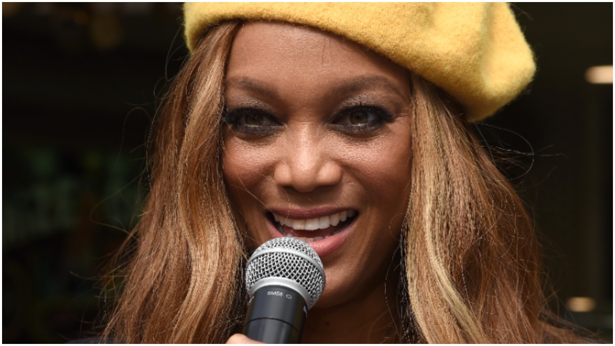 tyra banks wears a yellow hat while holding a microphone