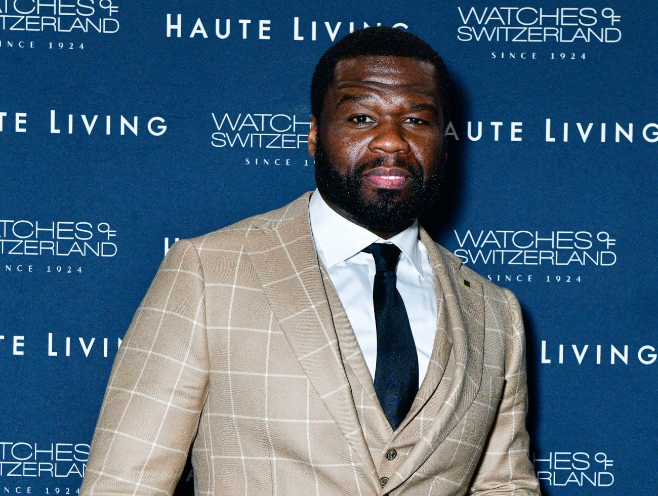 Curtis ‘50 Cent’ Jackson wearing a tan suit standing in front of a blue background.