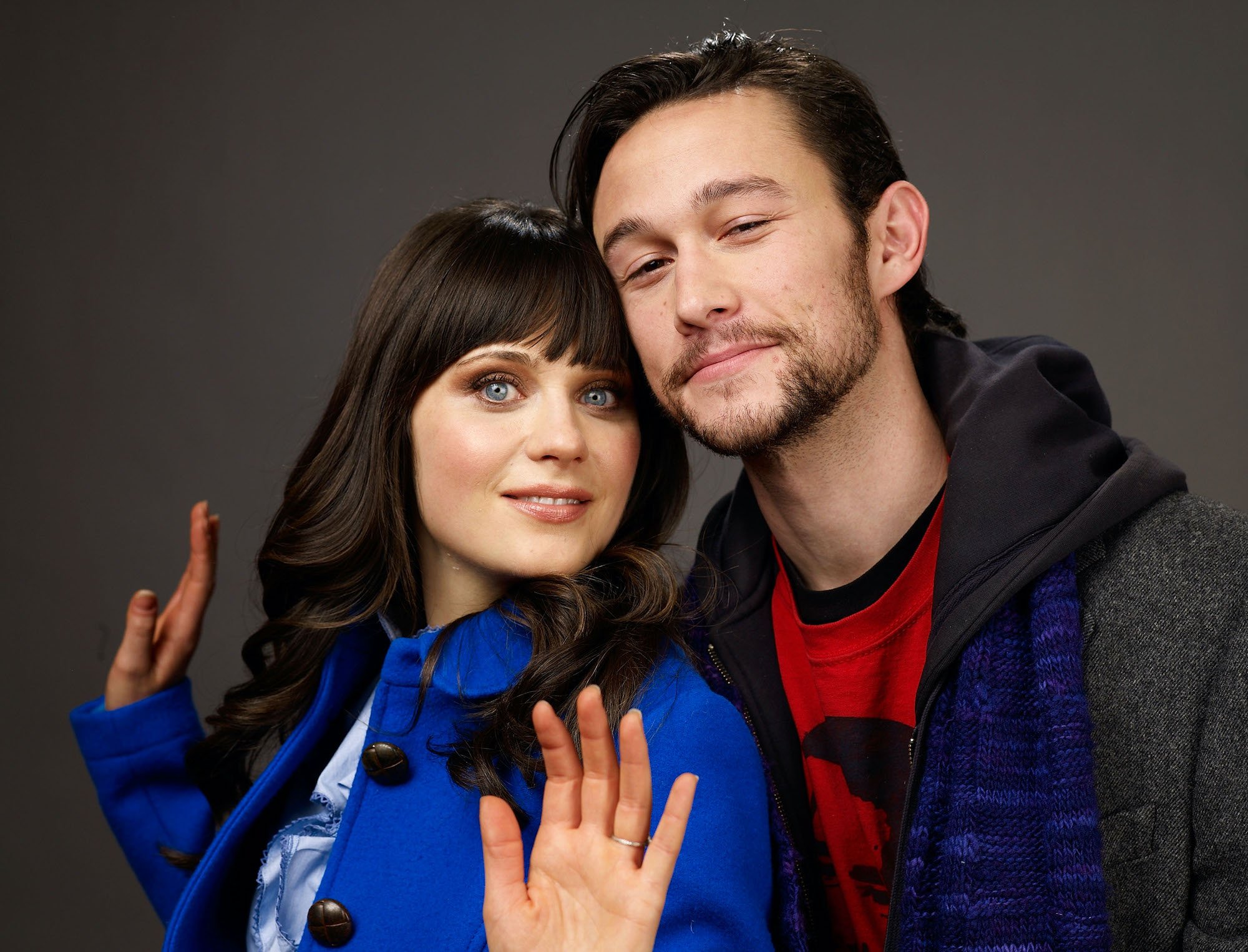 Zooey Deschanel and Joseph Gordon-Levitt smiling in front of a gray background