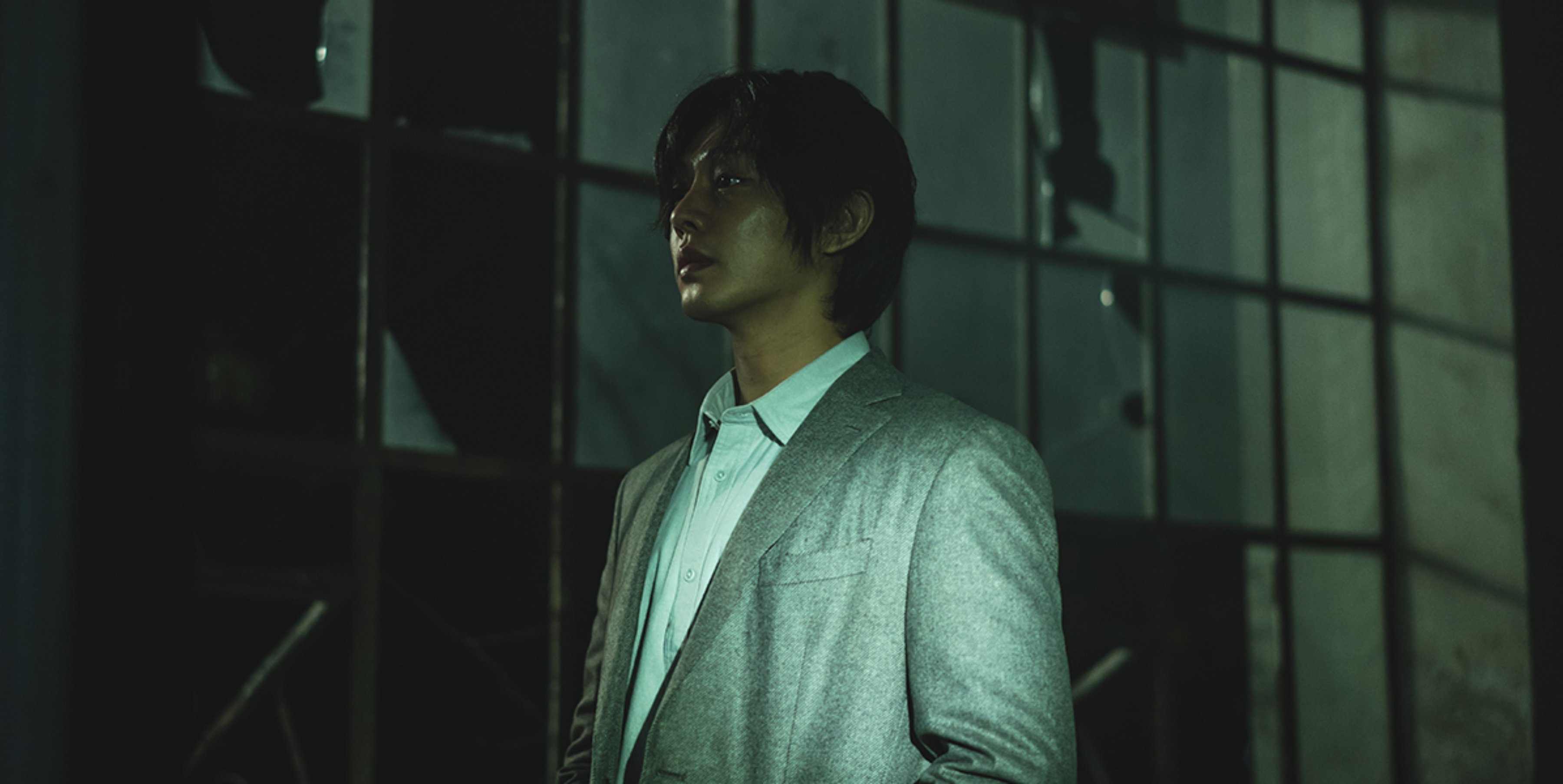 Actor Yoo Ah-In for Netflix's 'Hellbound' in dark lit room wearing grey suit and white shirt