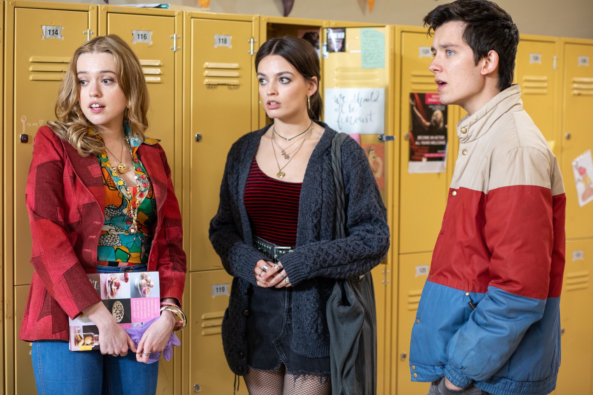 Aimee Lou Wood, Emma Mackey, and Asa Butterfield standing by yellow lockers in 'Sex Education' Season 2.