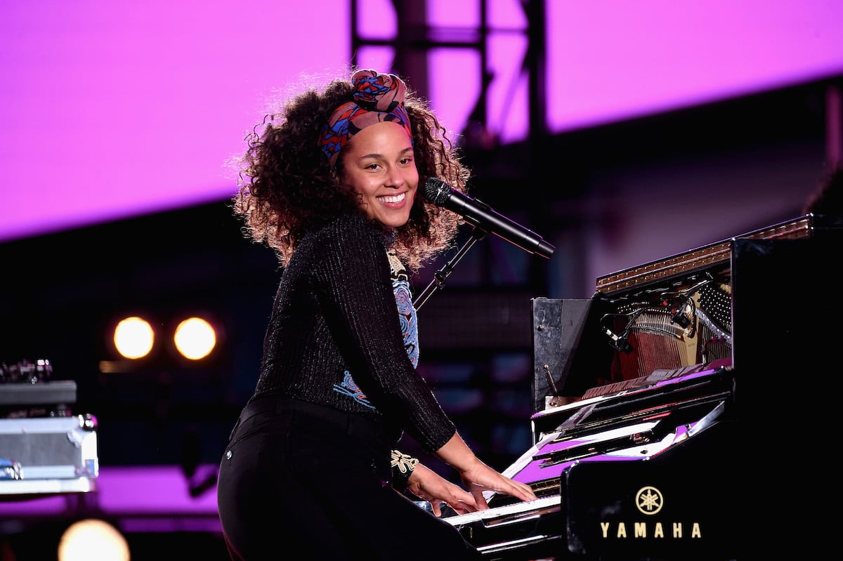 Alicia Keys wears all black smiling while playing the piano on stage at Times Square on October 9, 2016 in New York City.