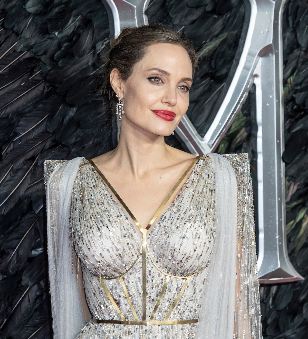 Angelina Jolie wears an embellished white gown and smiles for the camera at an event.