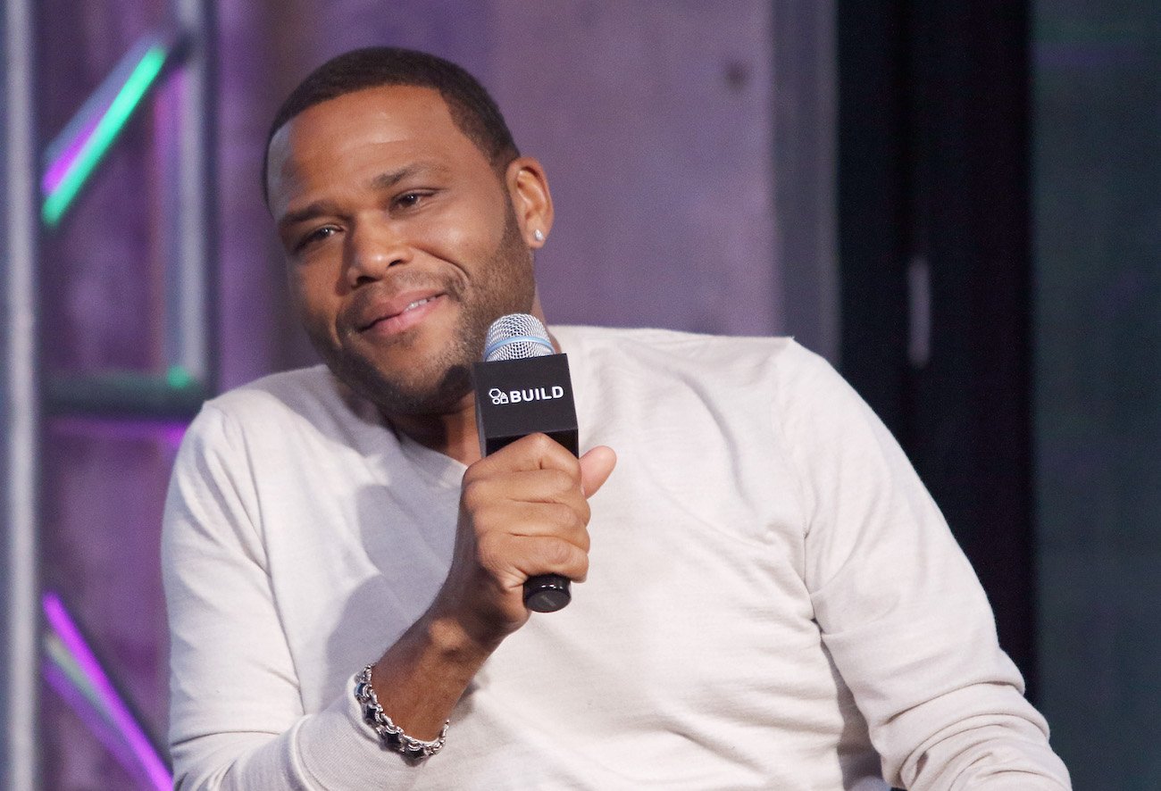 Anthony Anderson in a white shirt holding a microphone