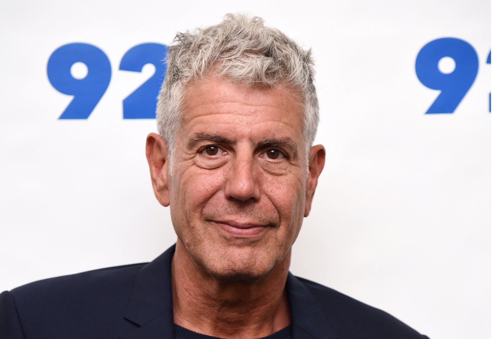 Anthony Bourdain smiling in front of a white background