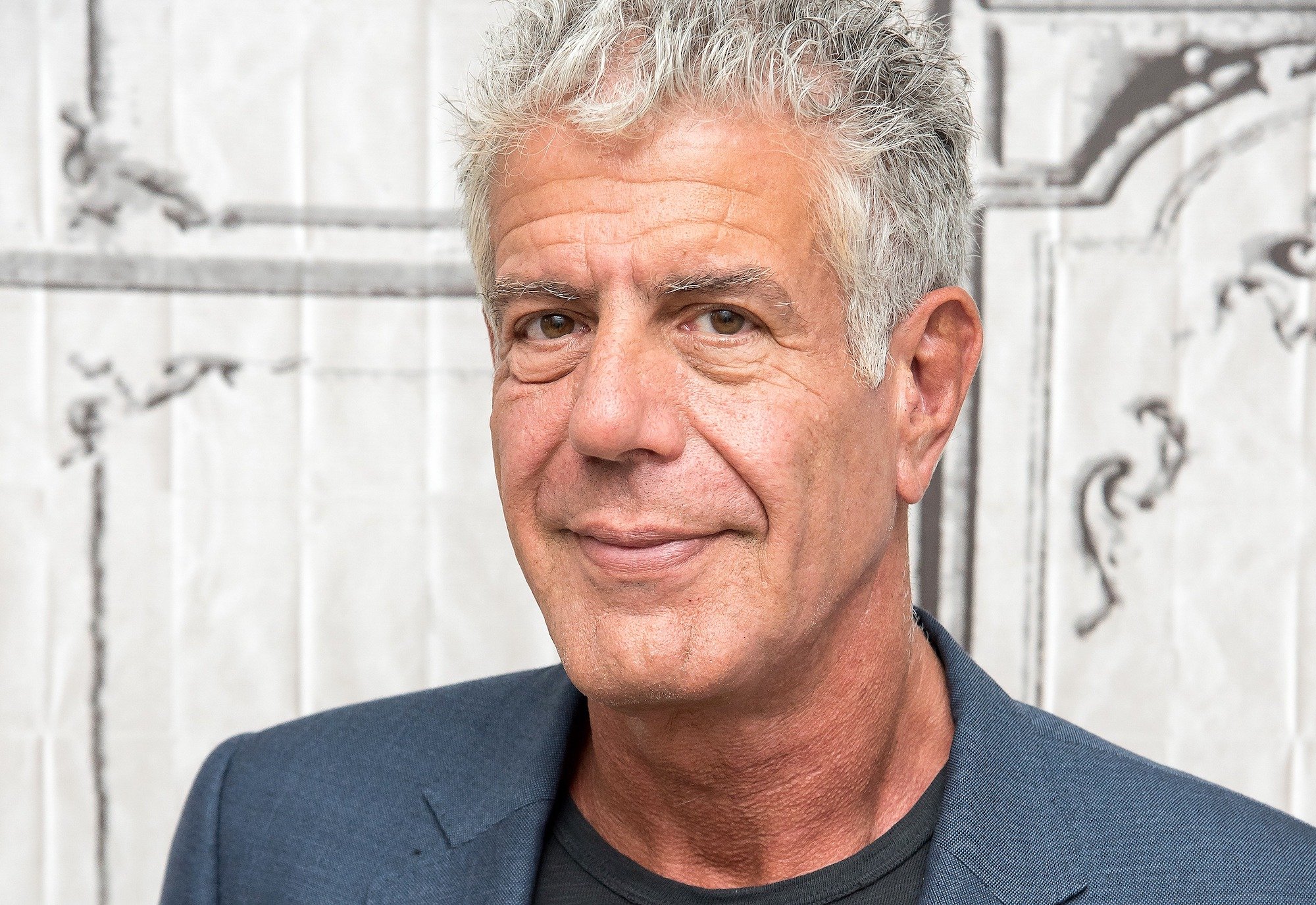 Anthony Bourdain smiling in front of a white background