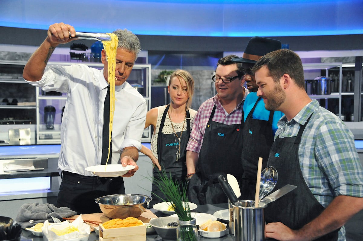 Anthony Bourdain uses tongs to remove pasta from a bowl as contestants on 'The Taste' watch