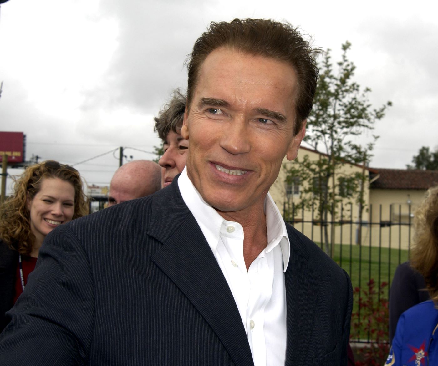 Arnold Schwarzeneggar standing in front of a podium dressed in a black suit.