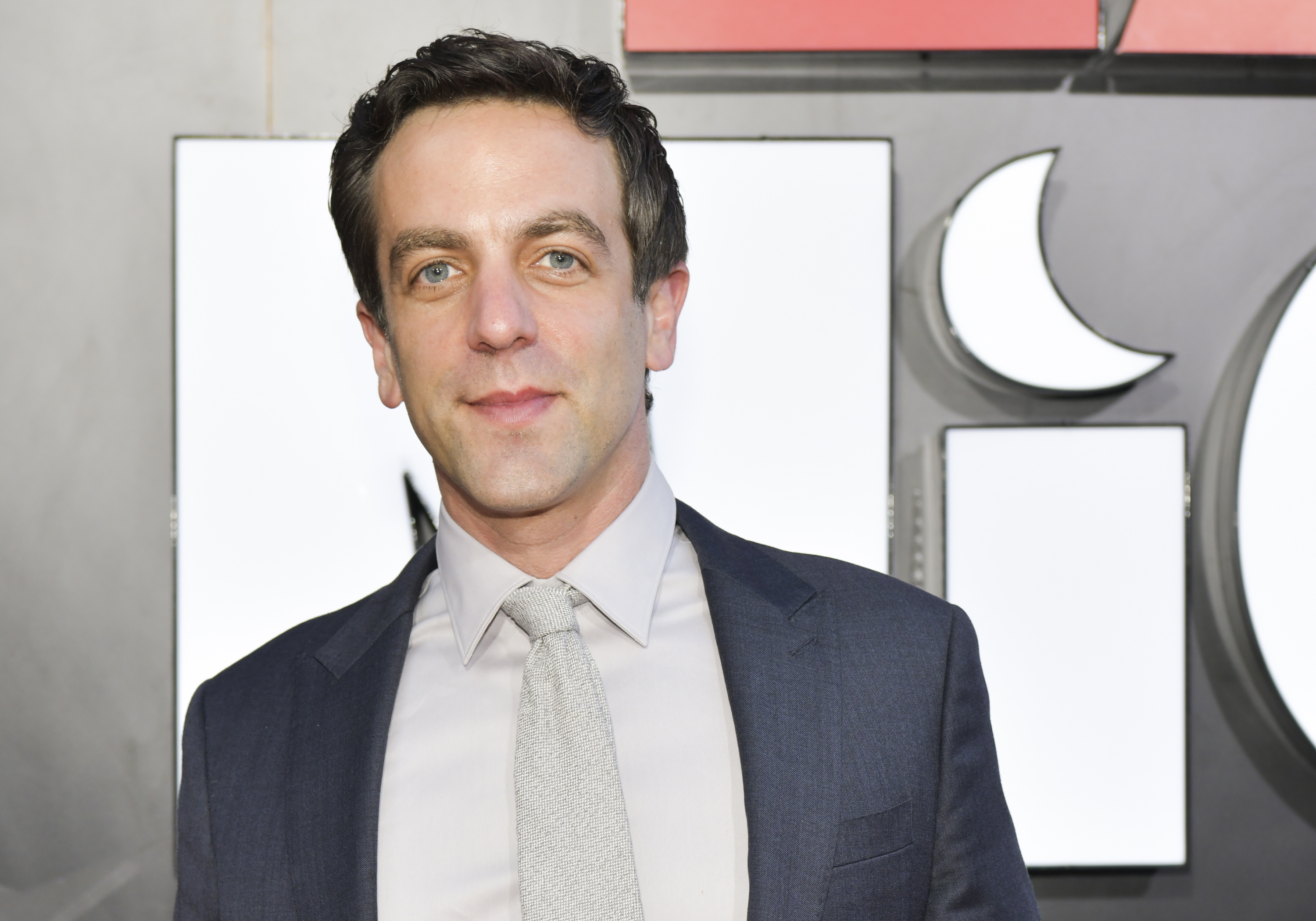 B.J. Novak smiles for a photo. He is wearing a suit and grey tie.