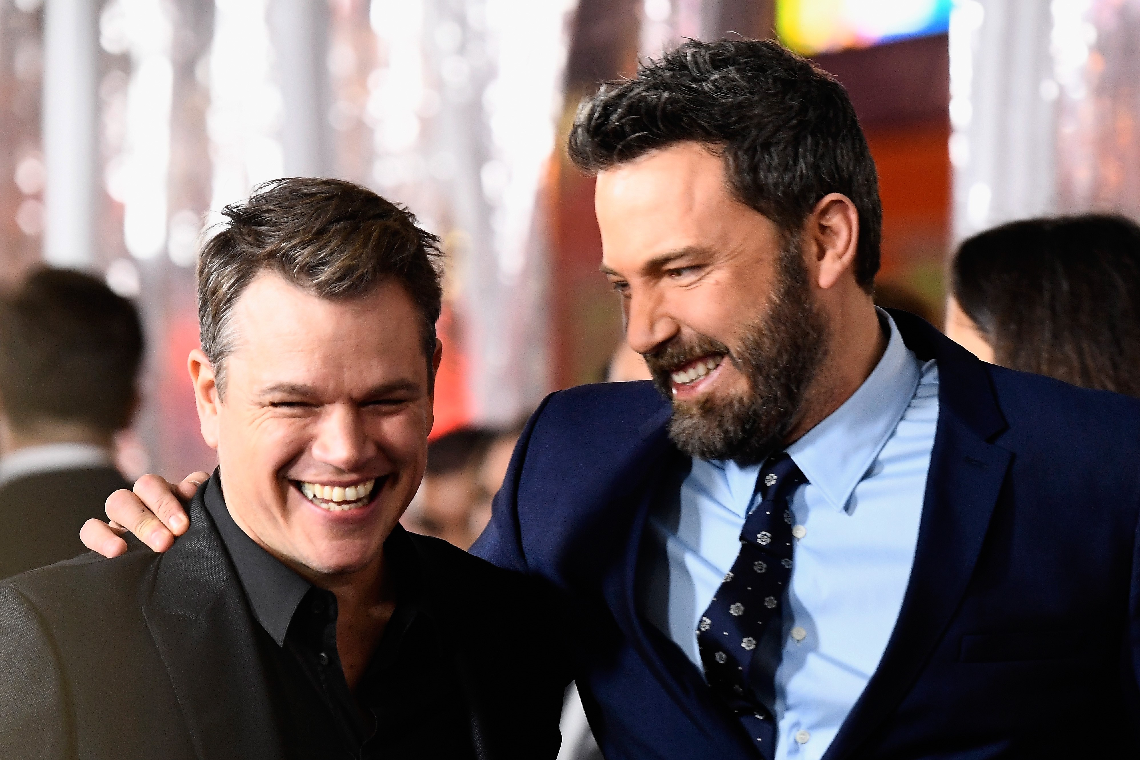 Matt Damon and Ben Affleck, in brown and blue jackets sharing a laugh, at the premiere of Warner Bros.' 'Live By Night' in 2017.
