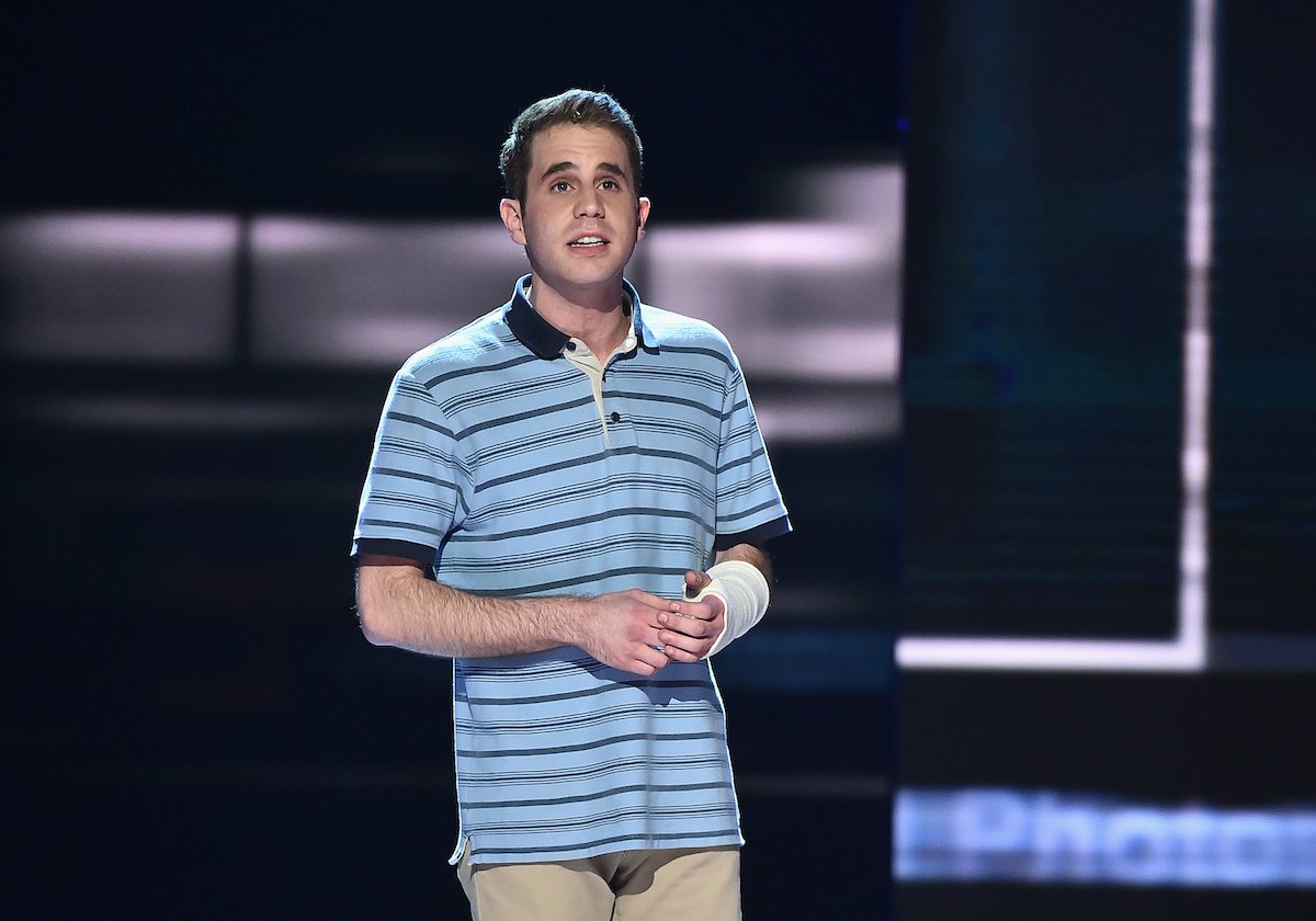 Ben Platt performing a song from 'Dear Evan Hansen' at the 2017 Tony Awards. He stands on a large stage wearing a blue, striped polo shirt and khaki pants with a white cast on his left arm. 