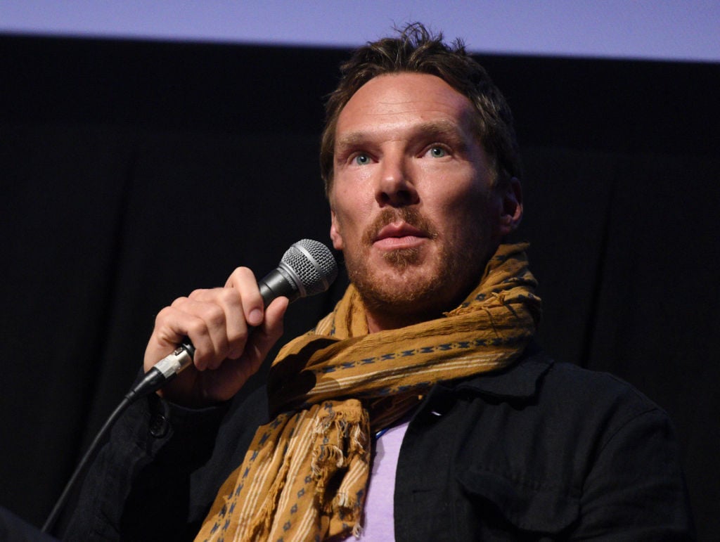 Benedict Cumberbatch holds a microphone. He's wearing a mustard yellow scarf.