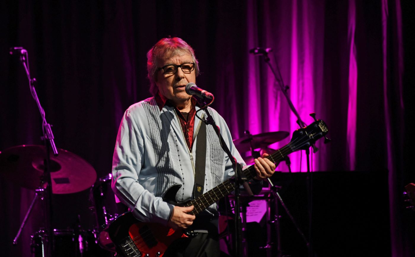 Bill Wyman performing at his 80th birthday in front of a purple curtain.