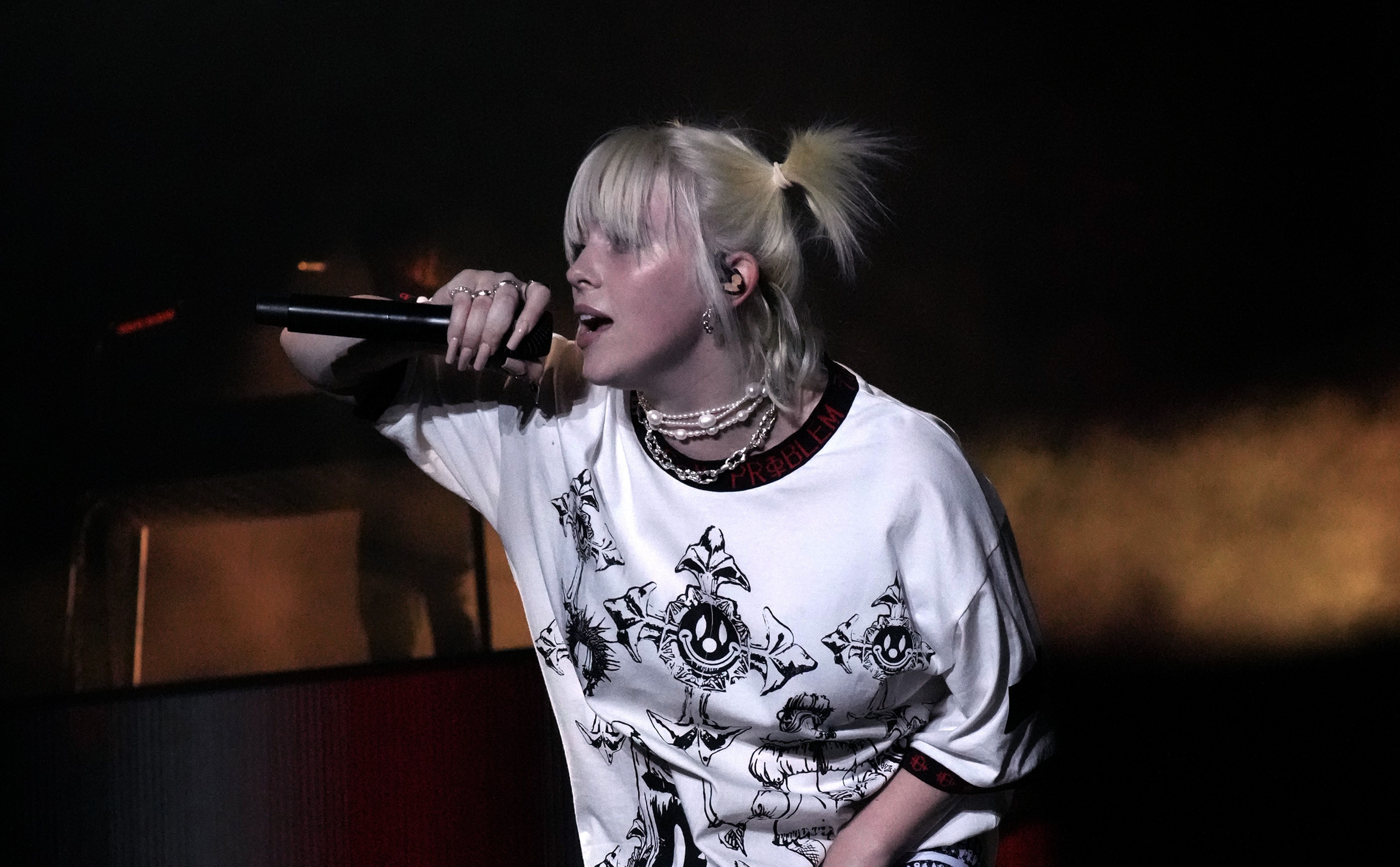 Billie Eilish sings on stage in a white T-Shirt and her short blond hair in high pigtails.
