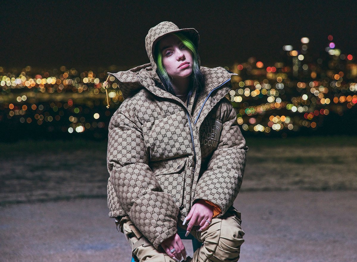 Billie Eilish wears an oversized puffy coat and scowls at the camera.