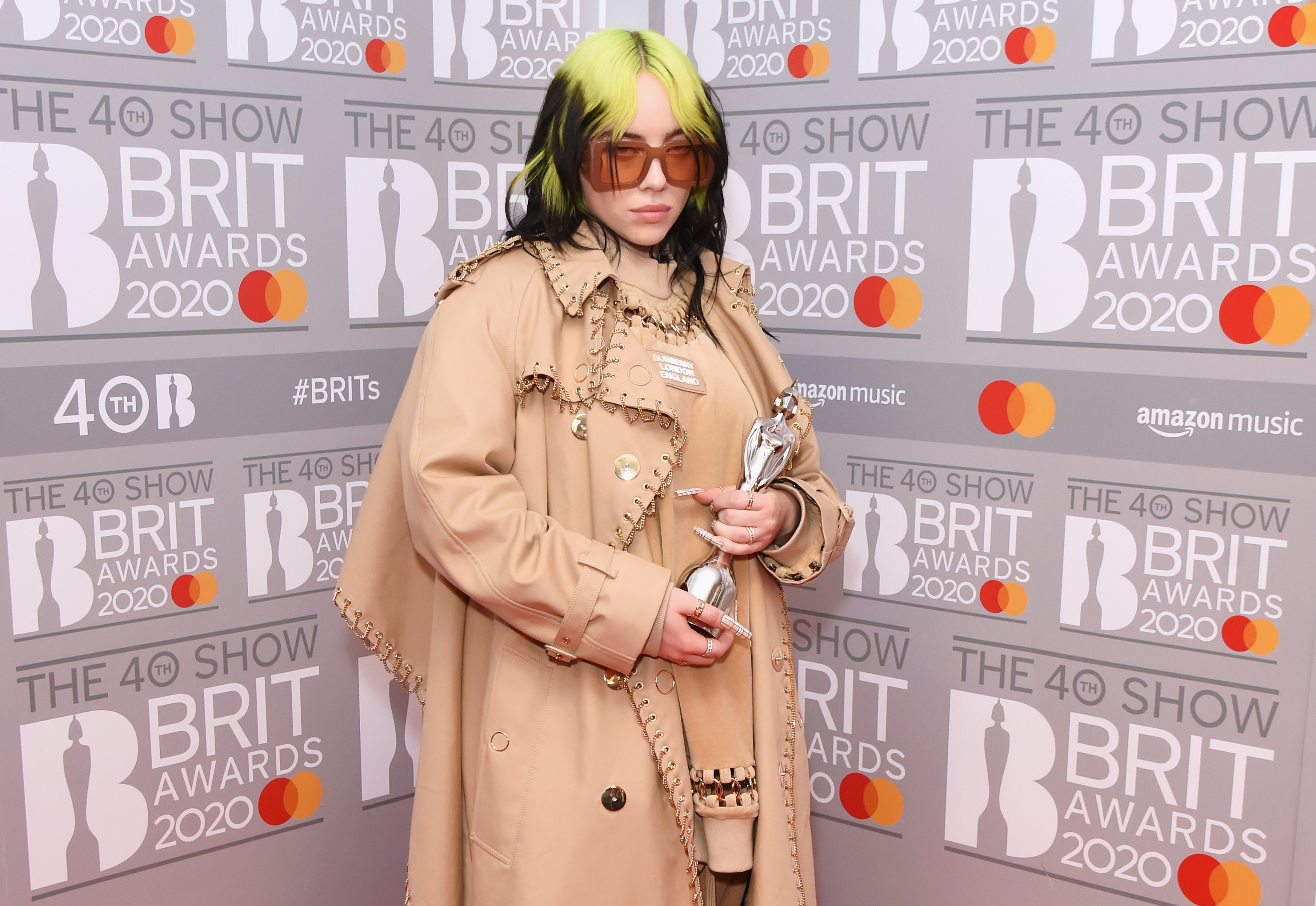 Billie Eilish holding an award in front of a gray background