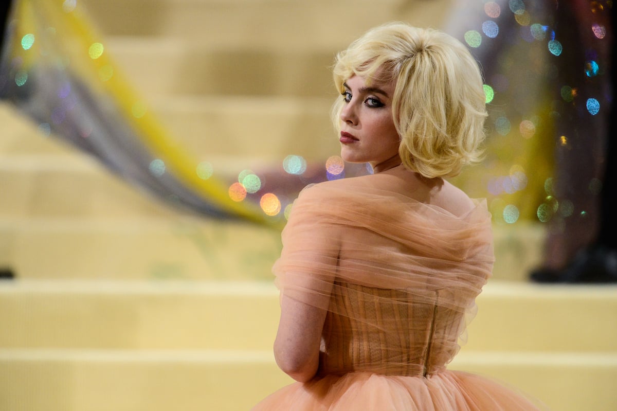 Billie Eilish looks over her shoulder at the camera., wearing a nude tulle ball gown.