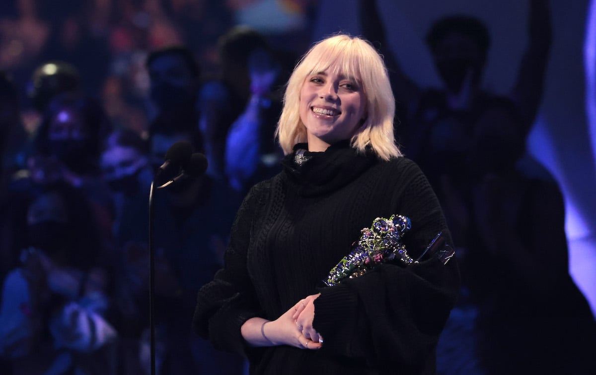 Billie Eilish cradles a VMA award on stage, smiling.