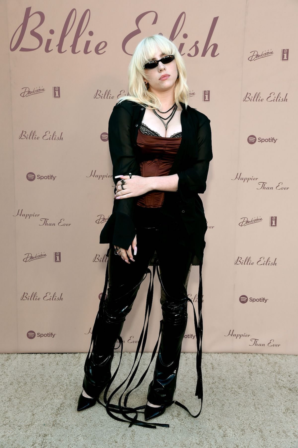 Billie Eilish wears a black outfit and sunglasses at an event.