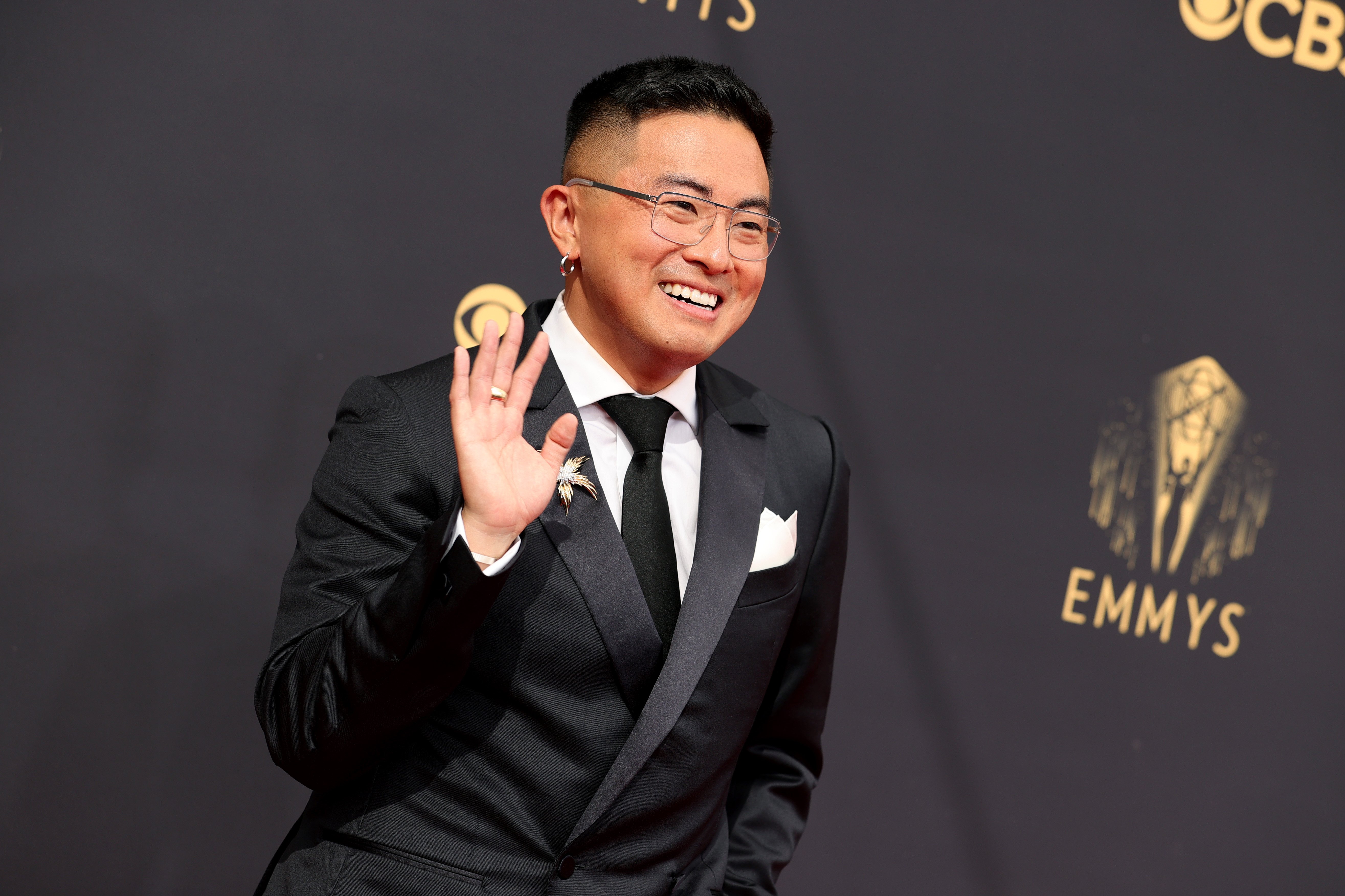 Emmy nominee Bowen Yang in a black suit, waving at the camera.