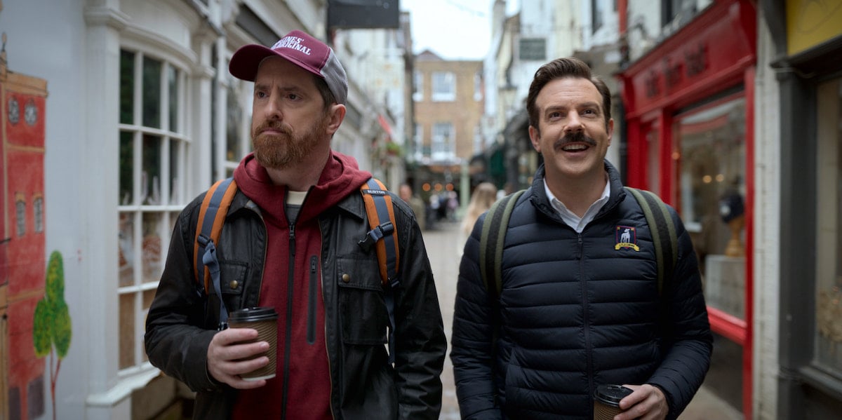 Brendan Hunt and Jason Sudeikis hold coffee cups as they walk down a street as Coach Beard and Ted in 'Ted Lasso' Season 2.