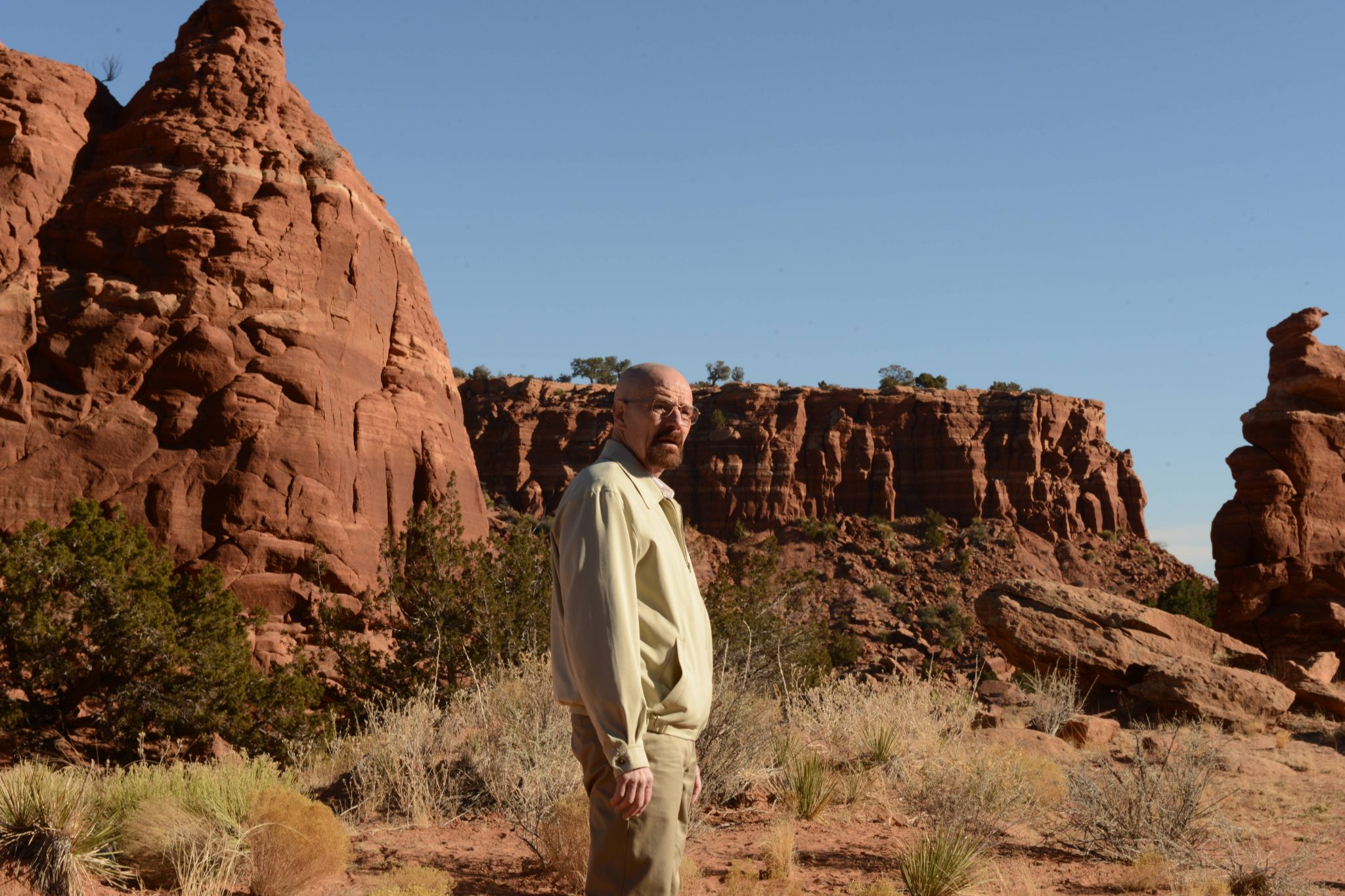 Bryan Cranston as Walter White  stands in a beige jacket and pants in the desert.