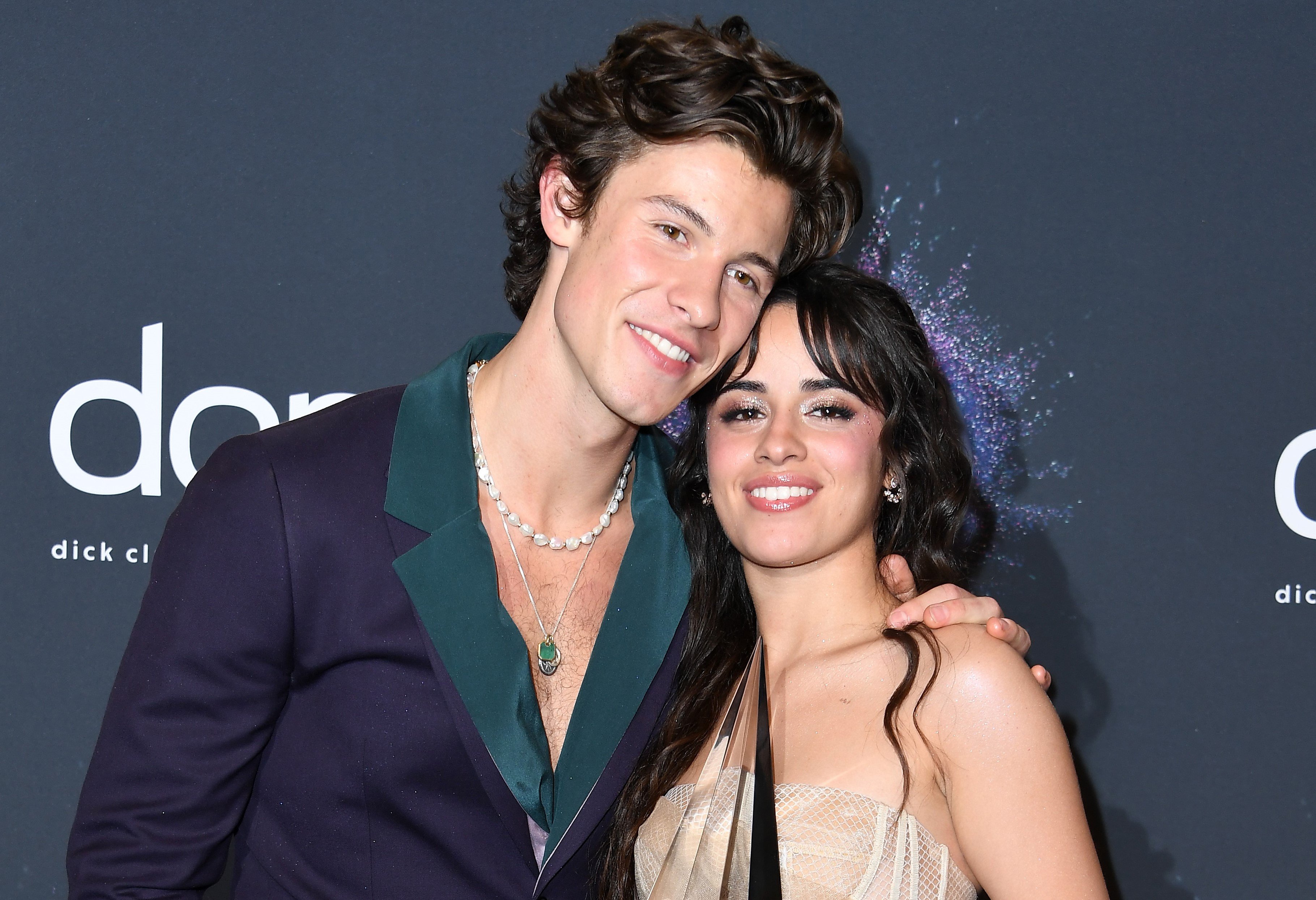 Shawn Mendes in a blue and green suit and Camila Cabello in a tan dress.