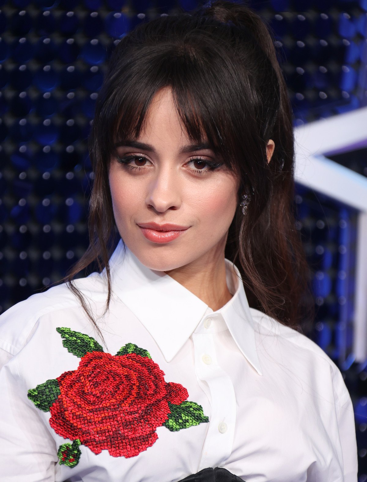Camila Cabello wears a white top with a large red rose on it at an event.