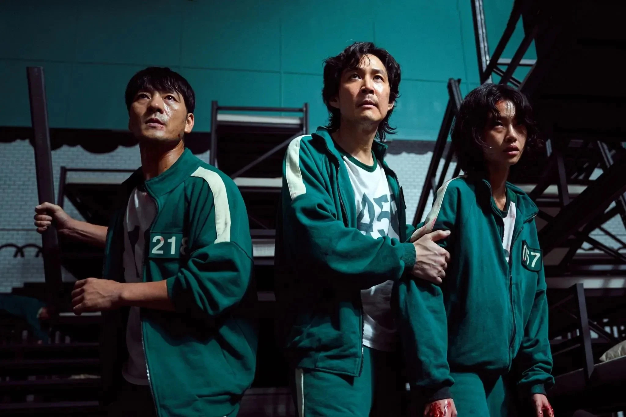 Characters Cho Sang-Woo, Seong Gi-Hun and Abdul Ali in 'Squid Game' wearing green tracksuits holding weapons