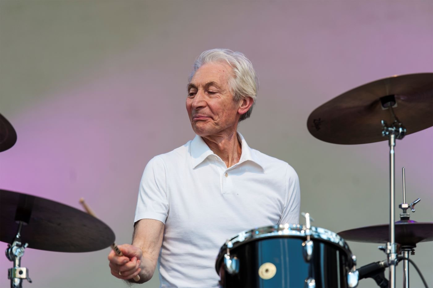 Charlie Watts playing a drum set in a white polo.