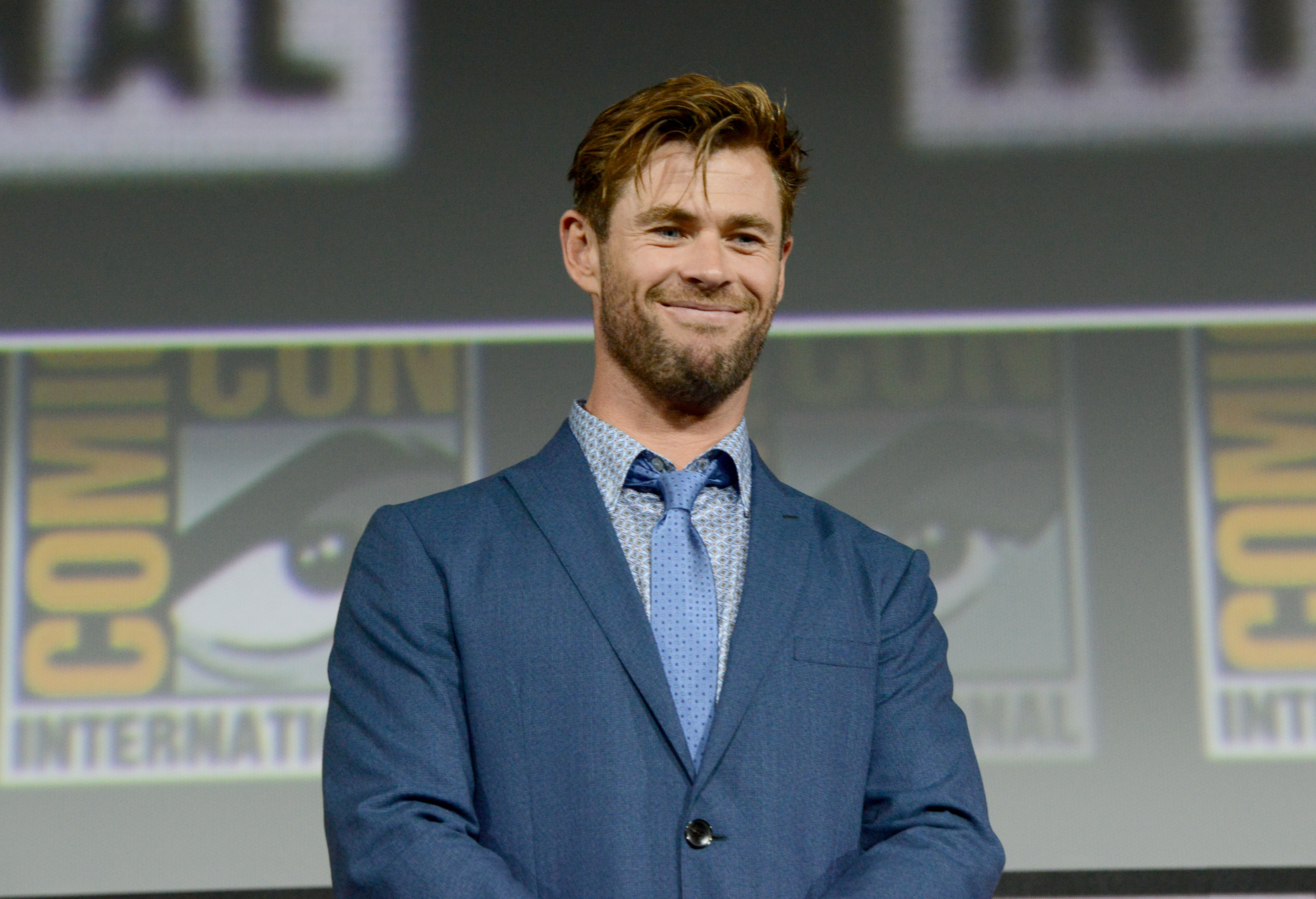 'What If...?' star Chris Hemsworth wears a dark blue suit over a light blue button down shirt and light blue tie.