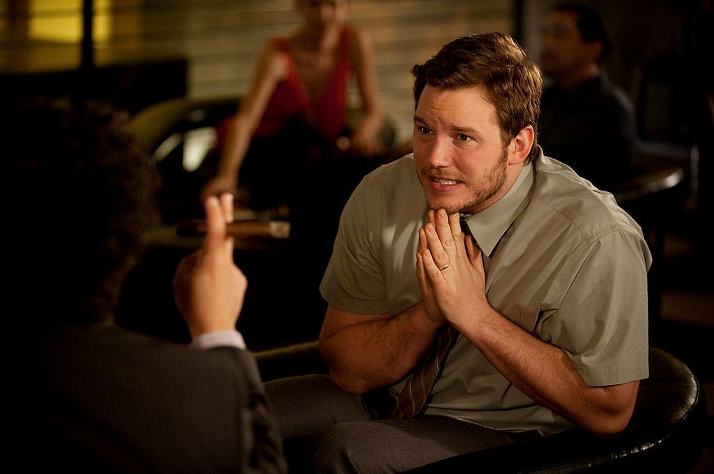 Chris Pratt as Andy is pleading with someone. His hands are folded as he sits across from an unknown person.