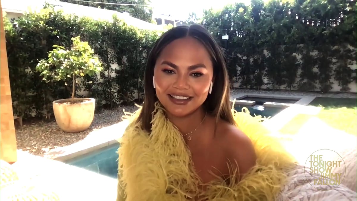 Chrissy Tegien smiles for the camera wearing a yellow feathered frock.