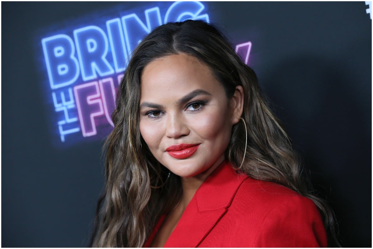 Chrissy Teigen smirking at the camera at a red carpet event.