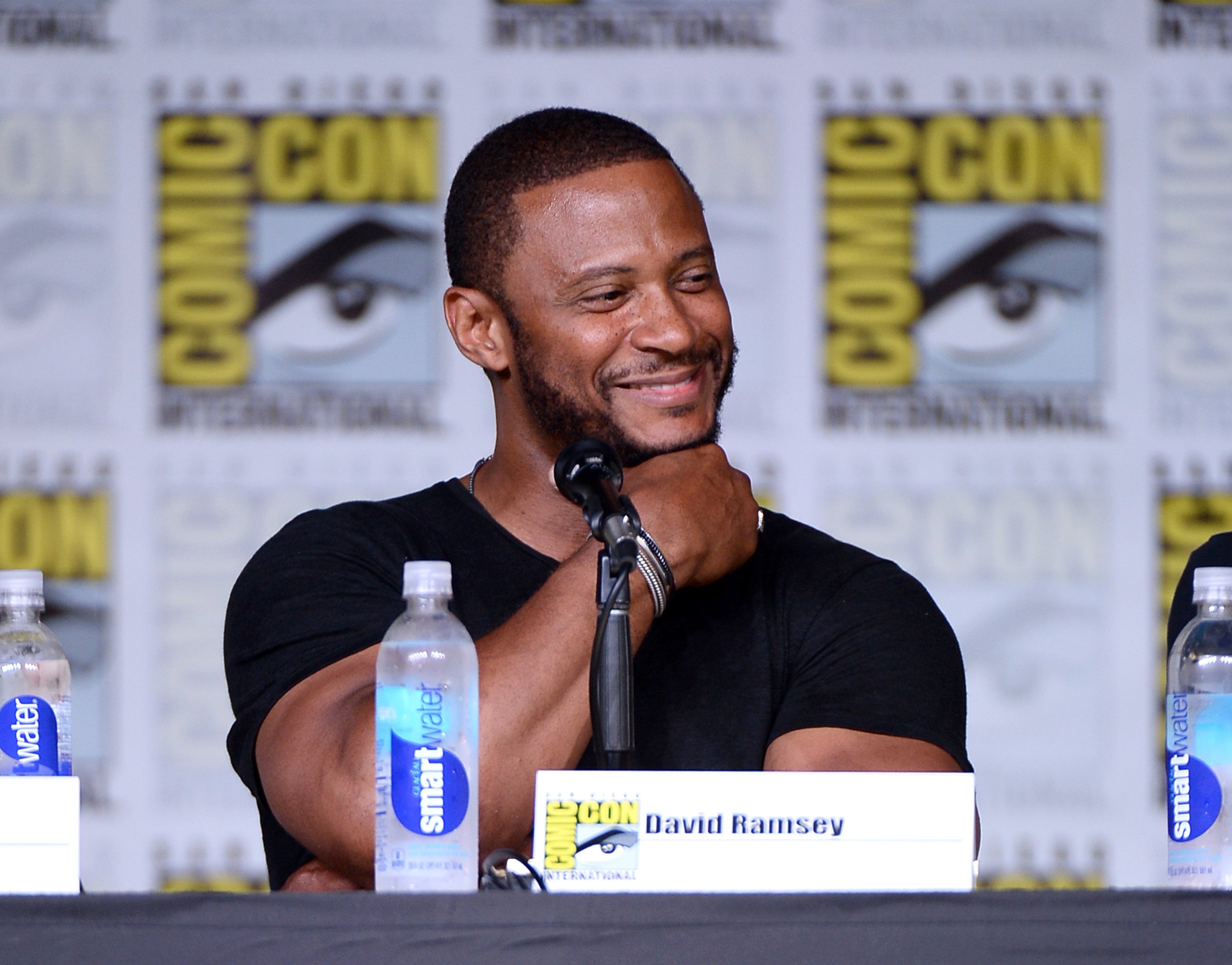 'Supergirl' special guest David Ramsey wears a black t-shirt and speaks at a Comic-Con panel.