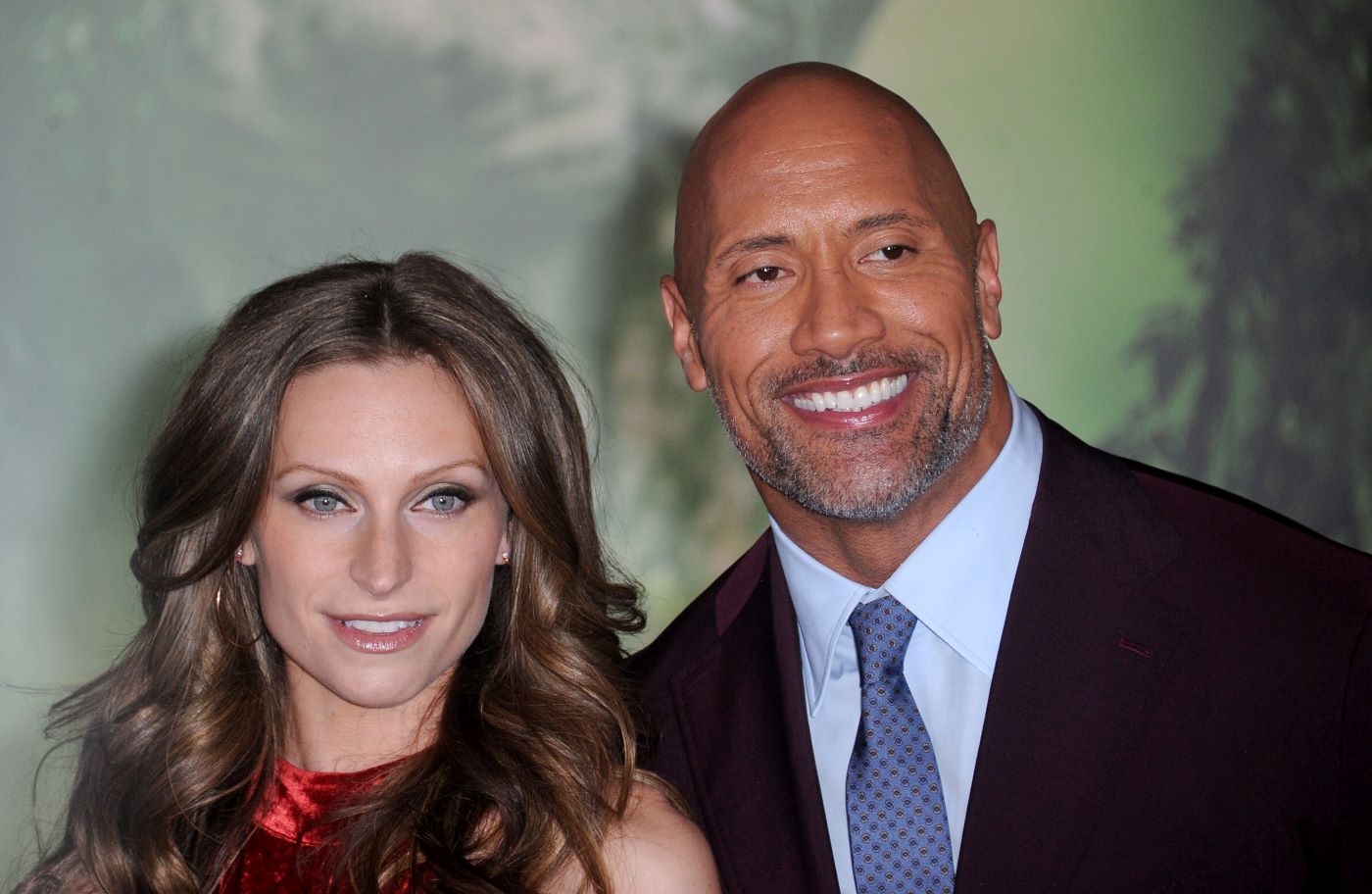 Dwayne Johnson and wife Lauren Hashian dressed professionally in front of a green background.