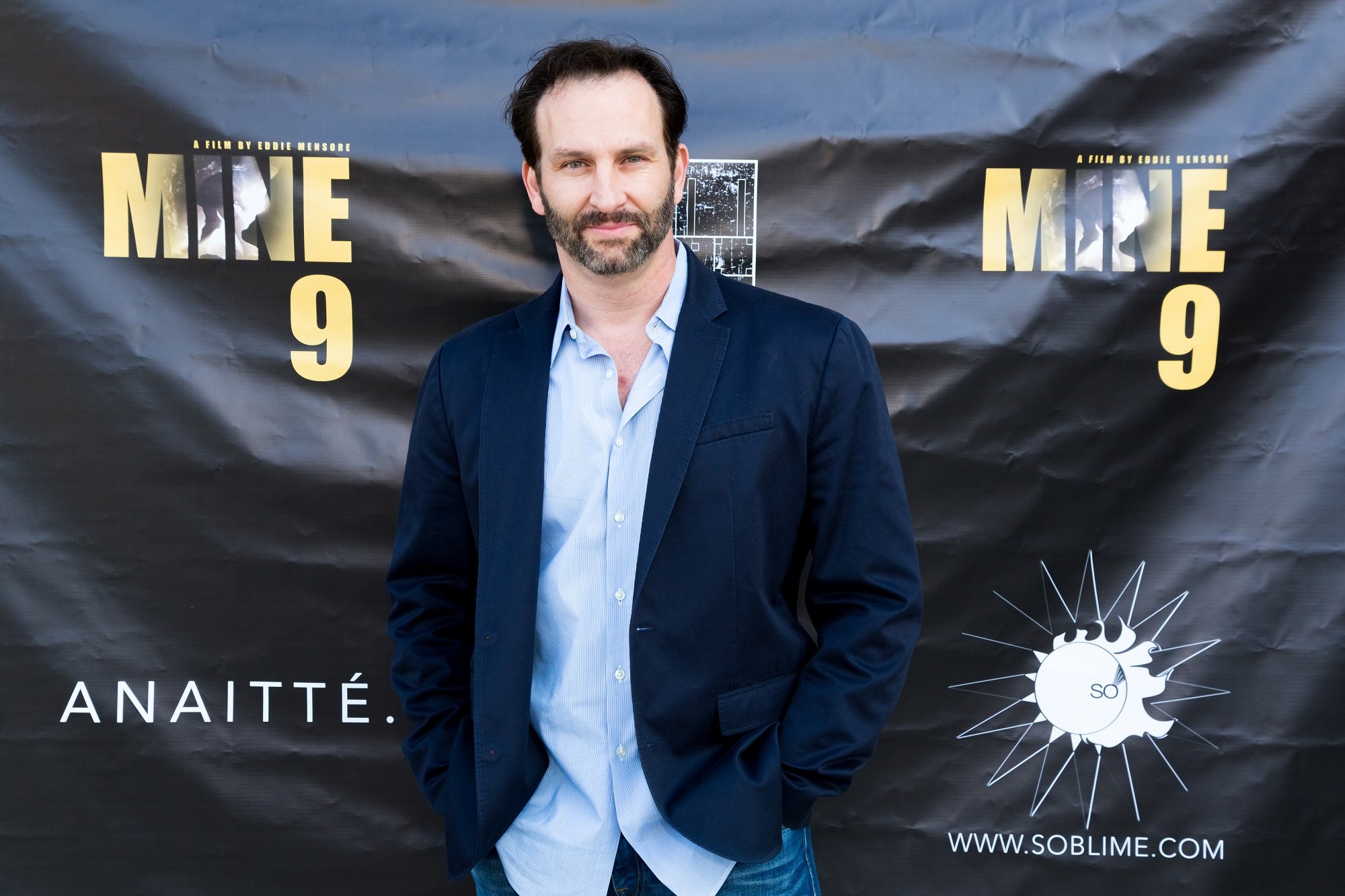 Days of Our Lives comings and goings focuses on Kevin Sizemore, pictured here in a black sweater and checkered shirt, on the red carpet against a black background
