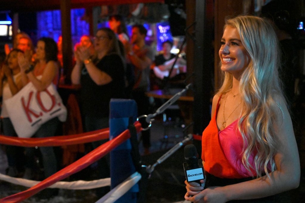 Demi Burnett holds a microphone while participating on 'The Bachelor'. She's wearing a red dress.