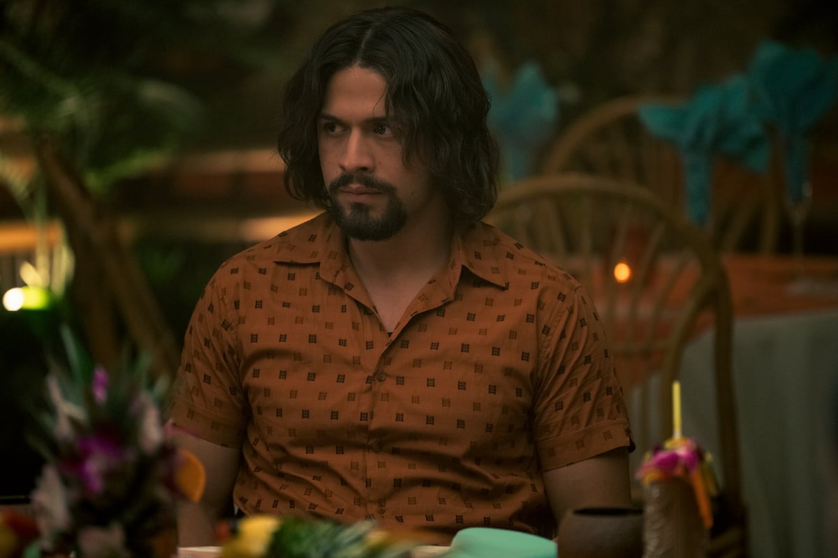 David Castañeda as Diego sitting at a table in an orange button down in a production still from 'The Umbrella Academy.'