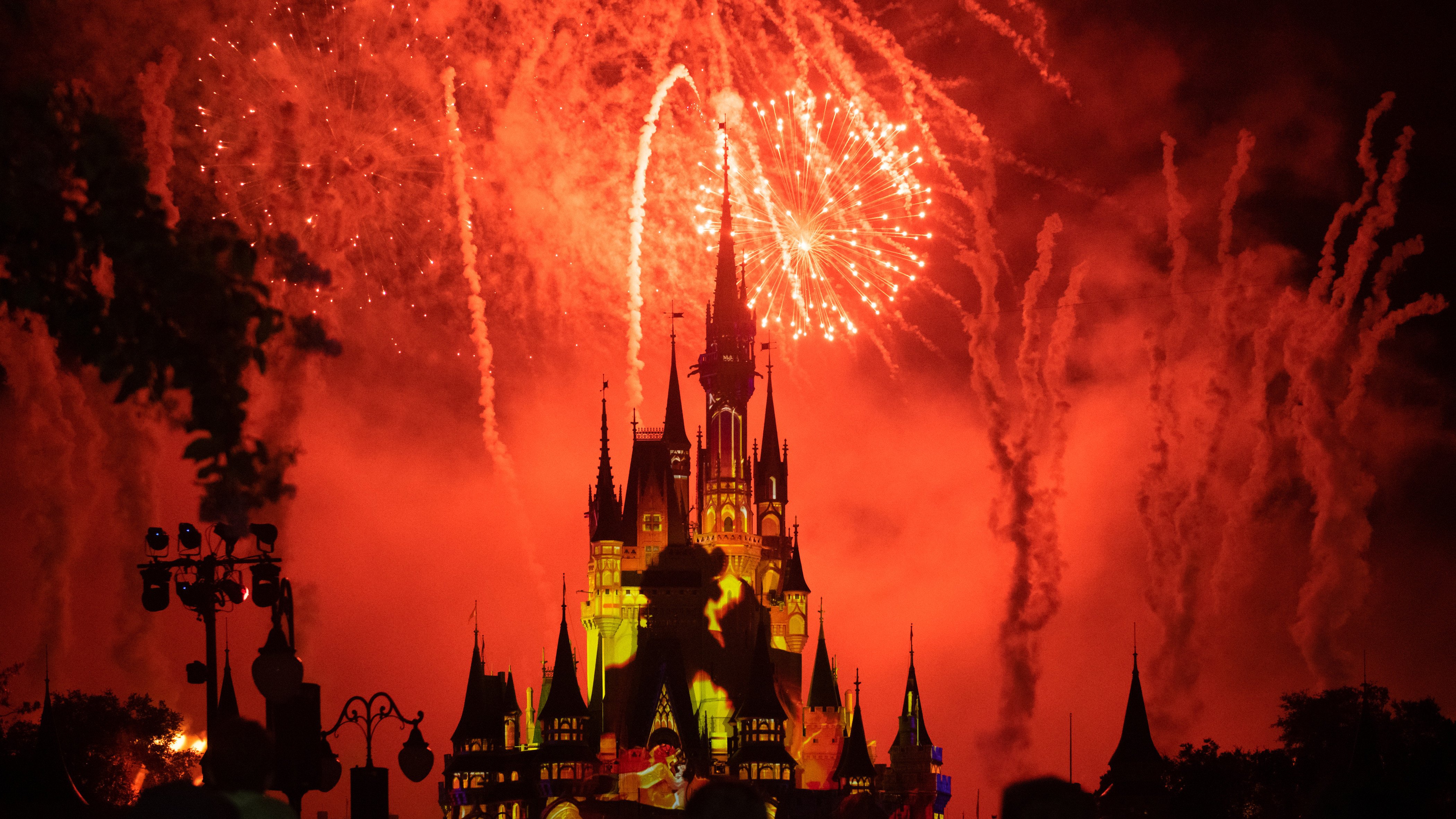 Red fireworks and yellow strobe lights illuminating the Cinderella Castle in the Walt Disney's Magic Kingdom themed park