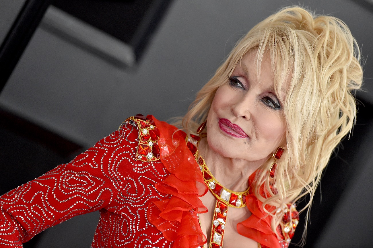 Dolly Parton wears a rhinestoned red dress. She once explained her support of Lil Nas X.