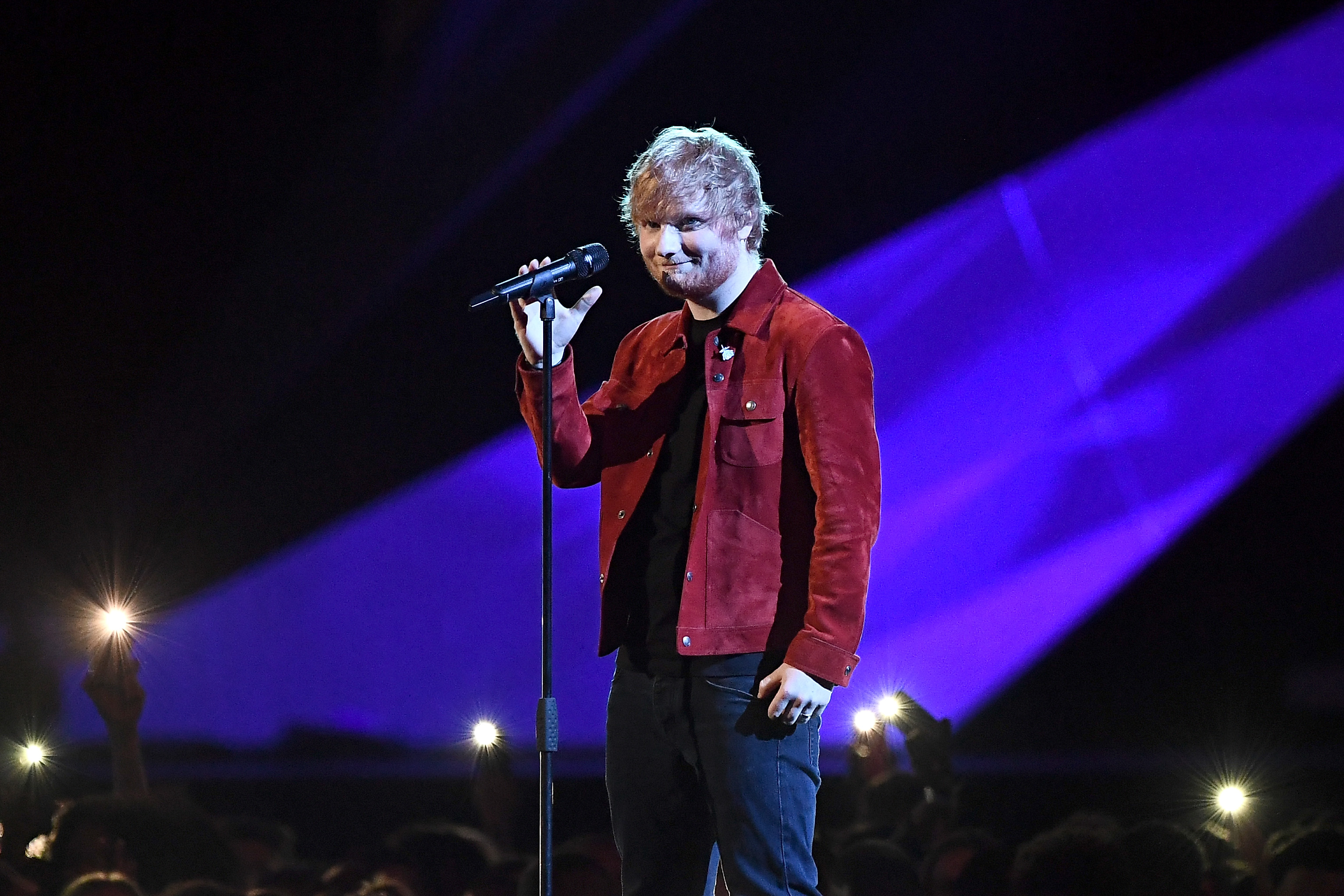 Ed Sheeran in a red jacket on stage at an awards show.