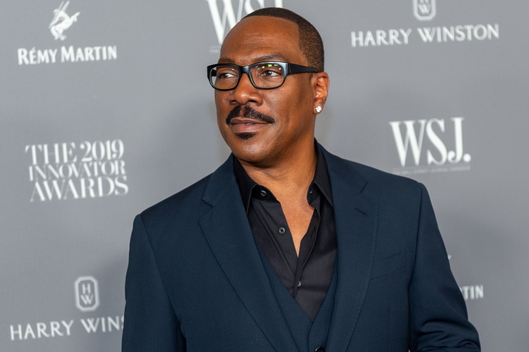 Eddie Murphy wears a navy suit in front of a gray backdrop